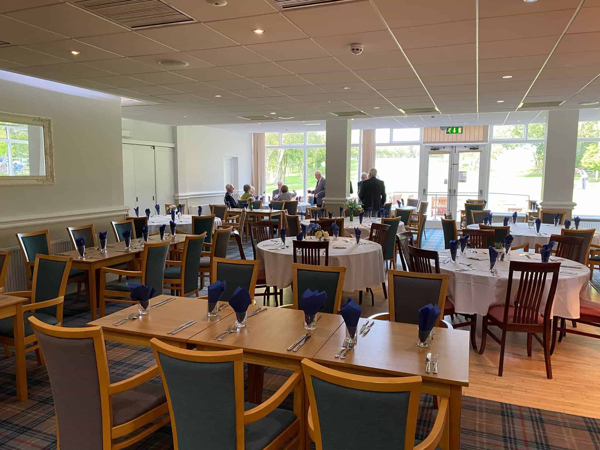The dining room at Horsforth Golf Club laid up for Sunday lunch, with white linen, folded napkins, and windows onto the golf course beyond.