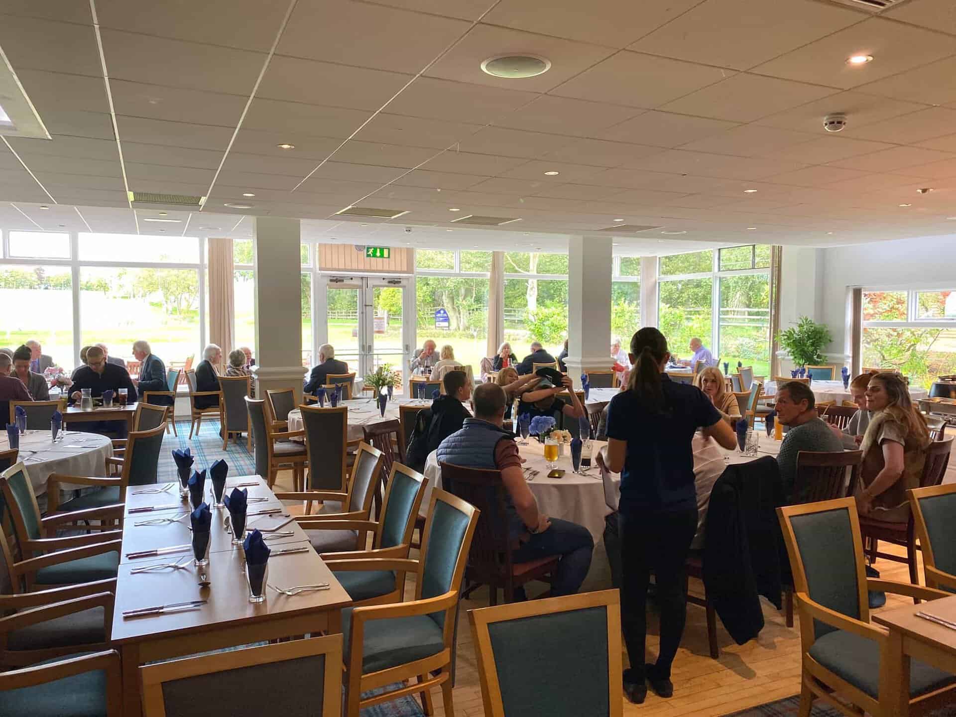 A busy Sunday service in the dining room at Horsforth Golf Club, with tables of guests eating and floor-to-ceiling windows looking out over the course.